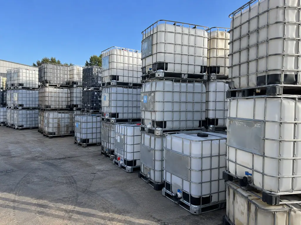 Rows of reconditioned IBC totes stacked two high across the yard under a clear sky